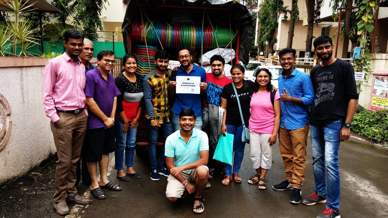 Approach volunteers standing in front of a truck loaded with relief supplies, holding a sign that reads Kerala & Karnataka