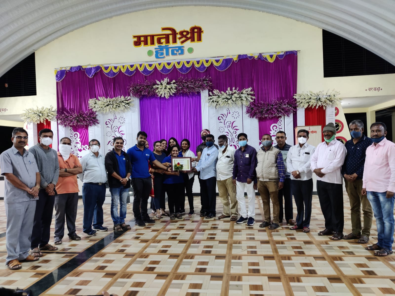 Men and women posing together on a decorated stage in Matoshree Hall.